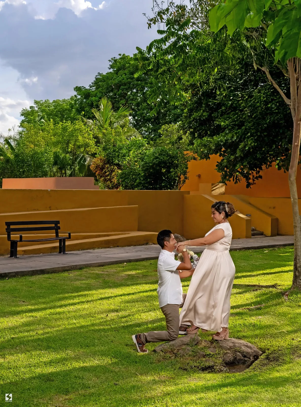 Novios en un parque junto a un muro naranja