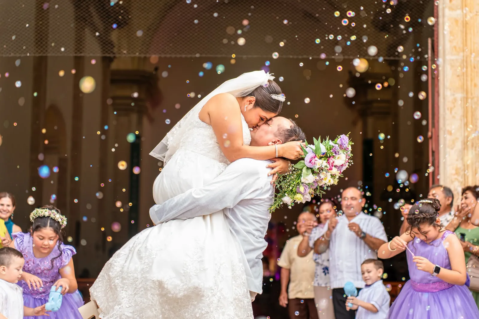 Novios besándose entre burbujas a la salida de la iglesia